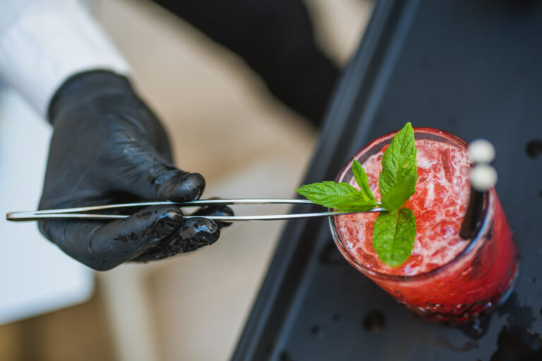 Close-up of a pink cocktail with fresh mint, lemon wedge and ice.