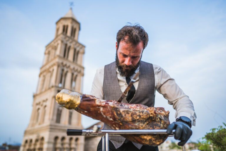 A waiter cutting prosciutto with the Cathedral in view